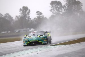 Green race car driving on a wet track with water spray during rainy weather.