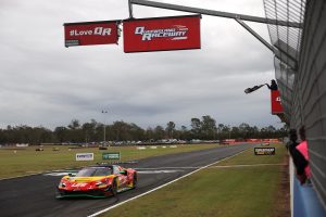 Race car crossing the finish line at Queensland Raceway as a checkered flag waves.
