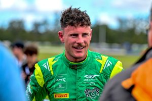 Race car driver in a green racing suit smiling at a motorsport event.