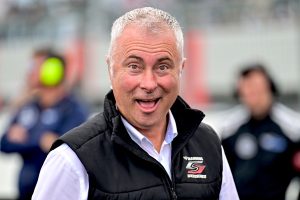 Smiling man wearing a racing team vest at a motorsport event.