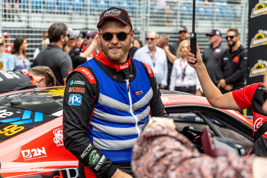 Brodie Kostecki, wearing a cool suit, stands next to his Erebus Camaro on the starting grid at the Supercars Gold Coast 500 in October 2023